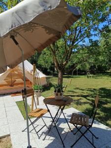 een tafel en twee stoelen en een paraplu bij Tente mongole " ô Rêves Atypiques" in Boucé