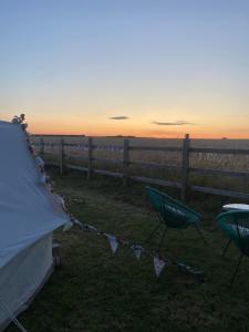 a tent and chairs in a field with the sunset at Country Bumpkins Luxury Glamping in Wellingore