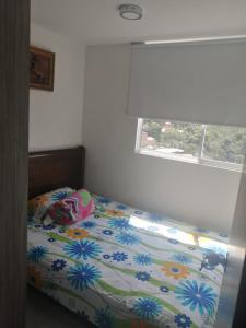 a bedroom with a bed with a floral comforter and a window at Apto Sabaneta 2 habitaciones al lado Centro Comercial Mayorca in Sabaneta