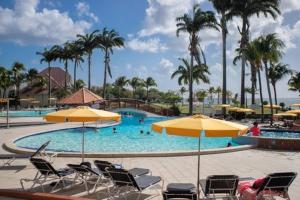 a swimming pool with chairs and umbrellas and palm trees at Studio dans un magnifique complexe de vacances a ST luce in Sainte-Luce