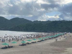 uma multidão de pessoas numa praia com guarda-sóis verdes em Nhà nghỉ Hưng Thơm em Ilha de Cát Bà