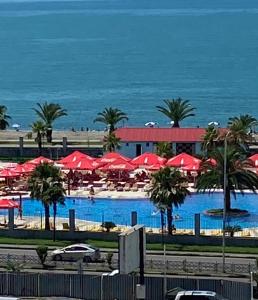 a resort with a swimming pool with red umbrellas and the ocean at Apartment Orbi Plaza Batumi in Batumi