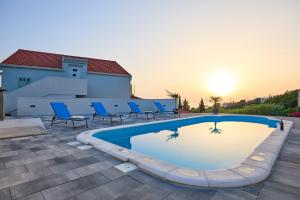 a swimming pool with blue chairs and the sunset in the background at Mia Maria Apartment in Cavtat