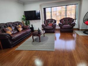 a living room with leather couches and a tv at Bed & Breakfast @ Unsworth Heights Albany in Auckland