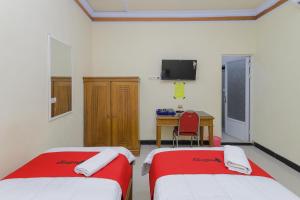 two beds in a room with a desk and a chair at RedDoorz Syariah near Alun Alun Pasuruan in Pasuruan