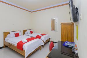 two beds in a room with a desk and a tv at RedDoorz Syariah near Alun Alun Pasuruan in Pasuruan