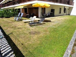 eine Terrasse mit Stühlen und einem Sonnenschirm auf dem Rasen in der Unterkunft Studio Valdor by Interhome in Crans-Montana