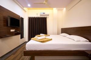 a bedroom with a bed with white sheets and a television at Hotel Ranjan Deluxe in Kolhapur