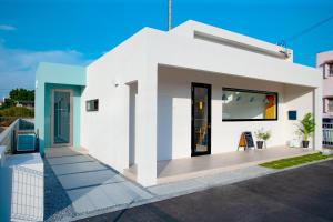 une maison blanche avec une terrasse couverte à l'avant dans l'établissement Hichu House ハイチューハウス, à Nago