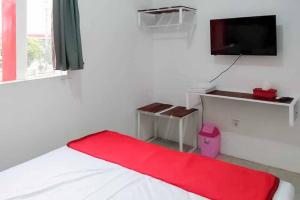 a bedroom with a bed with a red blanket and a tv at RedDoorz near Alun Alun Magetan in Magetan