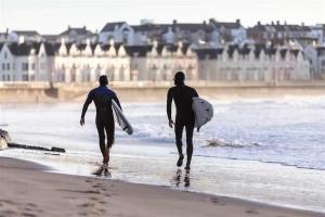 two men walking on the beach with their surfboards at 46 west strand avenue in Portrush