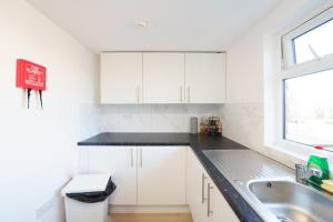 a white kitchen with a sink and a window at UB2 Suites - Heathrow London in Southall