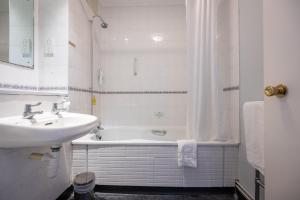Rising Sun Hotel by Greene King Inns في تشلتنهام: حمام أبيض مع حوض وحوض استحمام