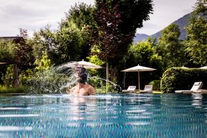 a man is in a swimming pool with a fountain at Superior Hotel Alpenhof in Flachau
