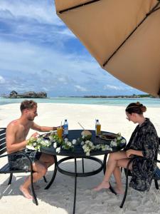 Ein Mann und eine Frau sitzen an einem Tisch am Strand in der Unterkunft FUNPLACE BEACH in Himmafushi