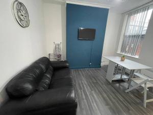 ein Wohnzimmer mit einem schwarzen Ledersofa und einem Tisch in der Unterkunft Joyous Private Room in City Centre in Liverpool