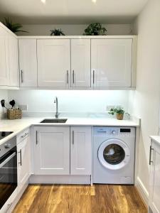 a white kitchen with a sink and a washing machine at Bright & Spacious 1 bed steps from Hyde Park in London