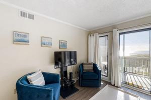 a living room with two chairs and a tv and a window at Dunescape Villas 221 in Atlantic Beach