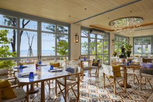a dining room with tables and chairs and windows at CHARRAS Bhawan Hotel and Residences in Hua Hin
