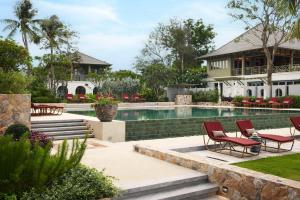 a swimming pool with two red chairs next to a house at CHARRAS Bhawan Hotel and Residences in Hua Hin