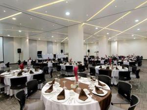 un salón de banquetes con mesas blancas y sillas negras en Ramada Encore by Wyndham Guadalajara Sur, en Guadalajara