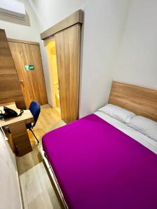 1 dormitorio con 1 cama grande de color púrpura y escritorio en Hostal Lumar, en Barranquilla