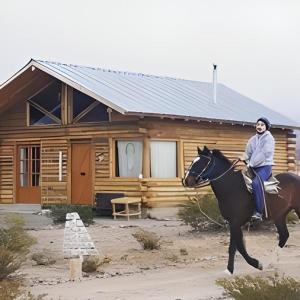 a woman riding a horse in front of a log cabin at cabañas de montaña in Uspallata