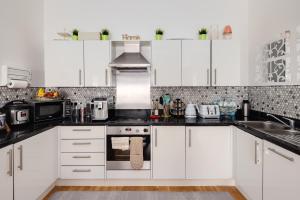 a kitchen with white cabinets and black counter tops at Two double bedroom duplex flat in London