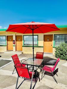 a table with red chairs and a red umbrella at Sage N Sand Motel in Moses Lake