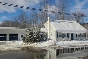 a white house in the snow with a reflection in the water at Vermont Farm House and Studio in Proctorsville