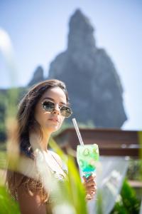 een vrouw met een zonnebril die een drankje met een rietje vasthoudt bij Dolphin Hotel in Fernando de Noronha