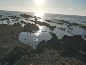 a beach with rocks and the ocean with the sun shining at Casa Dos Mosteiros in Mosteiros