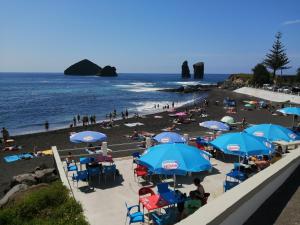 a beach with blue umbrellas and people on the beach at Casa Dos Mosteiros in Mosteiros