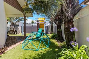 a blue spiderweb playground in a yard with a palm tree at Splash House at Kingscliff - Pet Friendly with Pool in Kingscliff