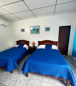 two beds in a bedroom with blue comforter at Hostal Villamil in Puerto Villamil