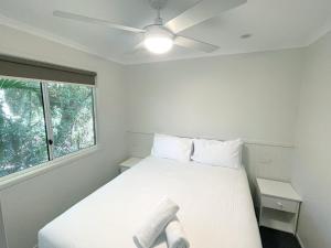 a bedroom with a white bed with a ceiling fan at Fingal Bay Holiday Park in Fingal Bay