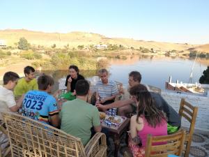 Seko Kato Nile View Hostel في أسوان: مجموعة من الناس يجلسون حول طاولة بجانب البحيرة