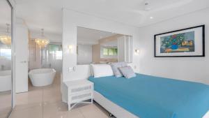 a white bedroom with a blue bed and a bath tub at Island Point Villa 1 Port Douglas in Port Douglas