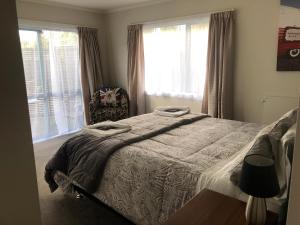 a bedroom with a bed and a chair and windows at Observation Holiday Home in Paraparaumu Beach