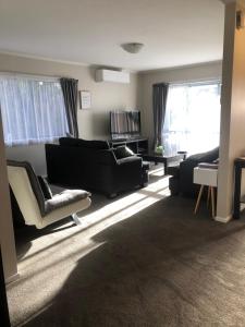 a living room with couches and chairs and windows at Observation Holiday Home in Paraparaumu Beach