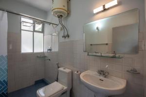 een badkamer met een wastafel, een toilet en een spiegel bij StayVista's Mystic Nest - Mountain & Valley-View Apartment with Contemporary Interiors & Modern Amenities in Gangtok