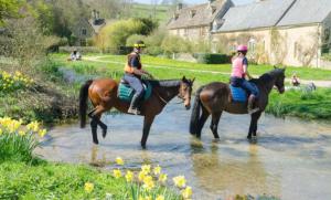 deux personnes à cheval dans l'eau d'une rivière dans l'établissement Jasmine Cottage, Upper Slaughter, Cotswolds, à Cheltenham