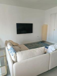 um sofá branco numa sala de estar com uma televisão de ecrã plano em La Casa Azul - next to the sea! em Torrenueva