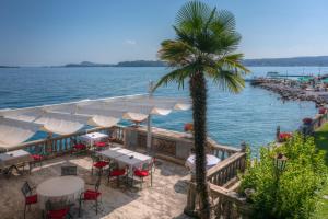 ein Strand mit Tischen und Stühlen und einer Palme in der Unterkunft Hotel Villa Capri in Gardone Riviera