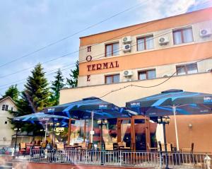 un grupo de mesas con sombrillas azules frente a un hotel en Hotel Termal, en Geoagiu Băi
