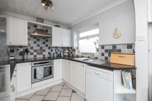 a kitchen with white cabinets and a sink and a window at Tan Y Wylan in Rhosneigr