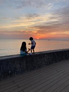 un niño y una niña sentados en una pared cerca del océano en Surfer's Cafe& Hostel, en Chatan