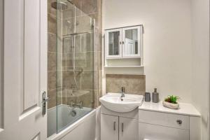 La salle de bains blanche est pourvue d'un lavabo et d'une douche. dans l'établissement Hidden Gem in Battersea w/ Free Parking, à Londres