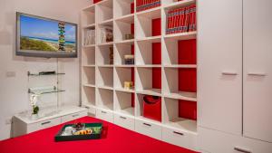 Zimmer mit weißen Regalen, einem TV und einem roten Boden in der Unterkunft Villa delle Sirene 6, Emma Villas in Valderice