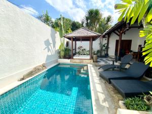 a swimming pool with two chairs and a house at Belharra Villas Seminyak in Seminyak